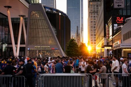 Massive crowd and police with security barriers outside Penn Station, NYC, at sunset.