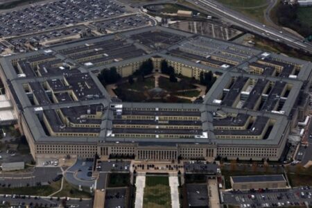 Aerial view of the Pentagon building, a large five-sided structure surrounded by parking lots and roads.