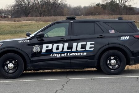 Black Geneva Police Department SUV patrol car parked on the side of a road with trees in the background.