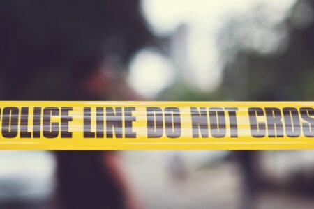 Yellow police tape with 'POLICE LINE DO NOT CROSS' written in black letters, against a blurred background.