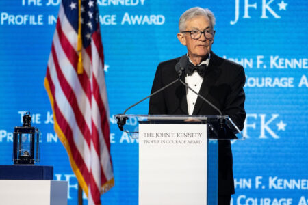 Former Fed Chair Jerome Powell speaks at a podium with an American flag and a JFK Profile in Courage Award backdrop.