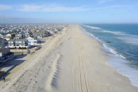 Aerial view of a New Jersey beach with ocean waves, sandy shore, and coastal houses under a blue sky.