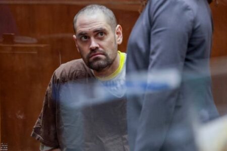 Nick Reiner, a man with a beard, looks up in a courtroom setting while a person in a suit stands nearby.