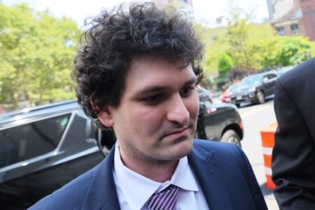 Sam Bankman-Fried, founder of FTX, looks serious in a suit outdoors, likely after a court proceeding.