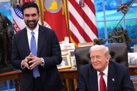 Donald Trump seated at a desk smiling, with a smiling man (Mamdani) standing beside him in an office.
