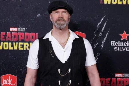 Actor Tyler Mane, with a beard and flat cap, poses in a pinstripe vest at an event.