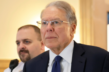 Former NRA CEO Wayne LaPierre in a suit and glasses, looking forward, with a man behind him.