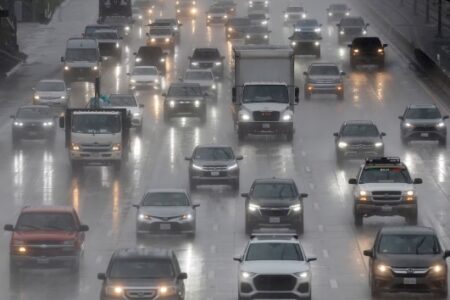 Cars and trucks drive on a wet highway in heavy rain, with headlights on.