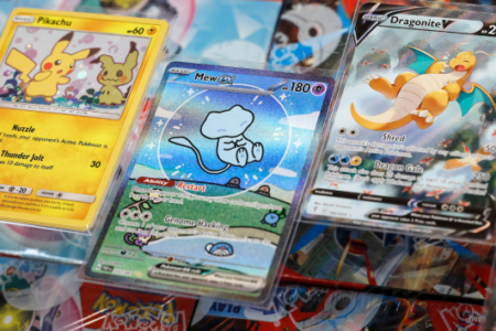 Close-up of three valuable Pokémon trading cards: Pikachu, Mew, and Dragonite V, in protective sleeves.