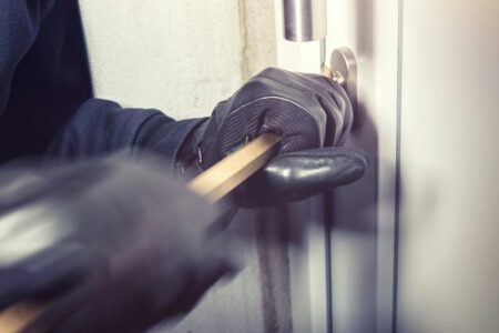 Gloved hands using a crowbar to force open a door, depicting a break-in.