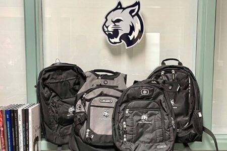 Several backpacks with the Jasper-Troupsburg High School wildcat logo are displayed in front of a window.