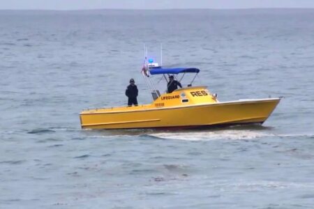 Yellow lifeguard boat with two crew members on choppy ocean waters during a search operation.