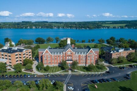 Aerial view of Keuka College campus with brick buildings, green lawns, parking lots, and a large lake in the background.