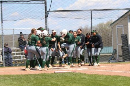 Keuka Wolves softball players in green uniforms celebrate on the field during a game.