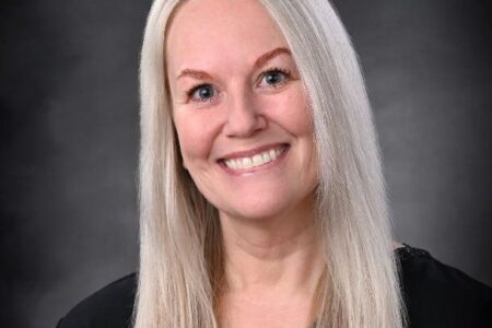Headshot of Michelle Beatty, a smiling woman with long blonde hair, wearing a dark top against a gray background.
