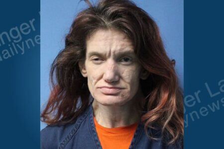 Mugshot of Michelle Travers, a woman with long brown hair and an orange shirt, against a blue background.