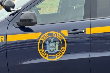 Close-up of a New York State Police patrol car door, showing the official seal and yellow stripe.