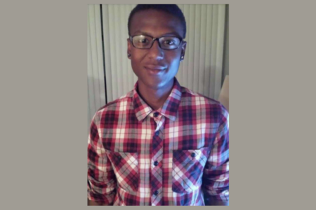 Elijah McClain, a young Black man in glasses and a plaid shirt, looks at the camera.