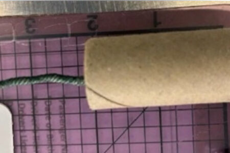 A small, cylindrical explosive device with a green fuse, shown on a ruler for scale.