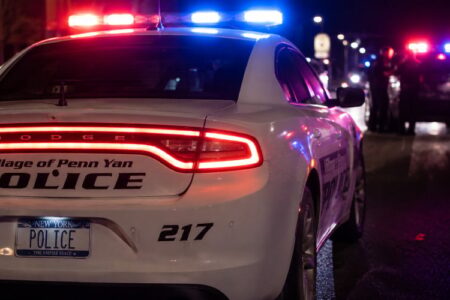 Rear view of a Penn Yan police car with flashing red and blue lights at night, another police vehicle visible in the background.