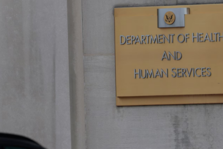 A close-up of the gold sign for the U.S. Department of Health and Human Services (HHS) on a stone building.