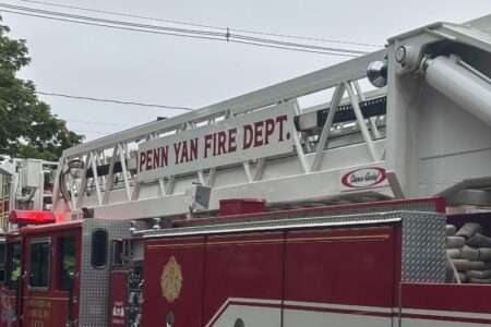 A red Penn Yan Fire Department ladder truck with its ladder extended against a cloudy sky.