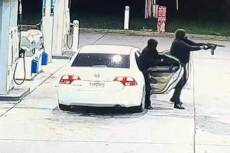 CCTV footage shows two masked gunmen exiting a white car at a gas station, one aiming a rifle.