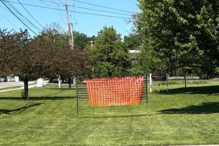 Grassy area with an orange barrier marking the proposed location for an electronic sign in Richmond, NY.