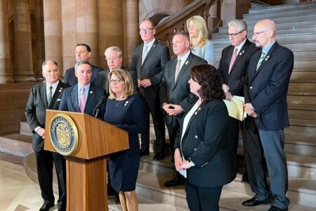 Senator Pam Helming speaks at a podium surrounded by other lawmakers, advocating for rural suicide prevention.