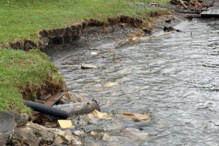 Eroded Seneca Lake shoreline with a drainage pipe and debris, indicating flooding impact.