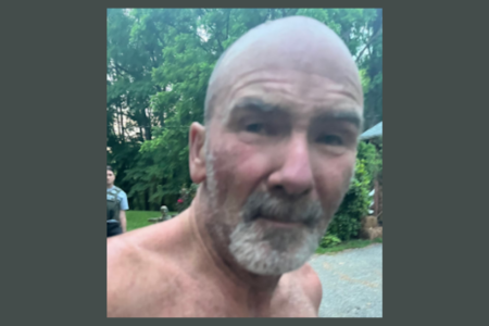 Michael Puckett, a bald, shirtless man with a gray beard, looks at the camera after his capture.