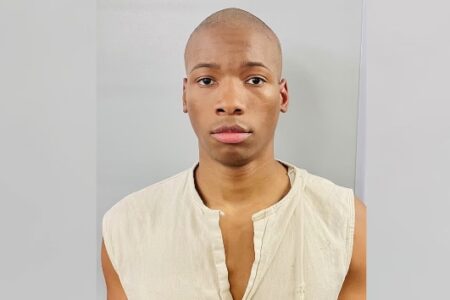Mugshot of Karmelo Anthony, a young Black man with a shaved head, wearing a light-colored sleeveless shirt.