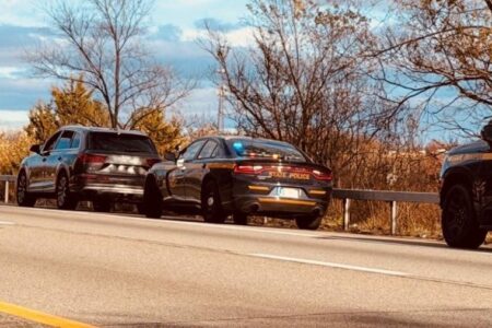 New York State Police car with lights on behind an SUV during a traffic stop on a highway.