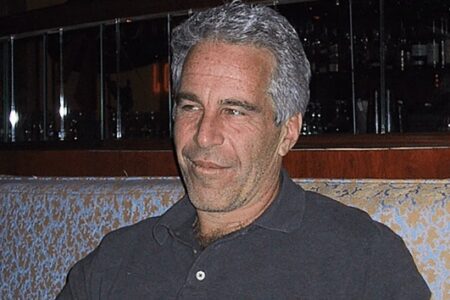 Jeffrey Epstein, a man with graying hair, sits on a patterned couch, looking slightly right with a faint smile.