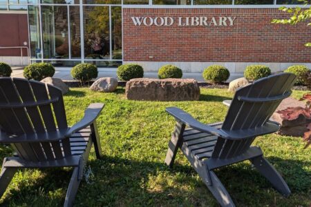 Exterior of Wood Library in Canandaigua with two Adirondack chairs on a sunny lawn.