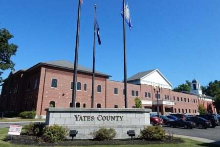The Yates County Office Building, a brick structure, with a sign, flags, and a clear blue sky.