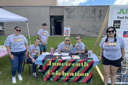 Six young people at an outdoor Juneteenth Celebration event booth, featuring a banner and informational display.