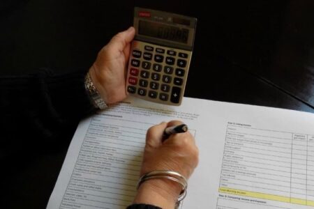 A person's hands working on a budget sheet with a calculator.