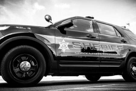 Black and white photo of a Cayuga County Sheriff's SUV parked outdoors under a cloudy sky.