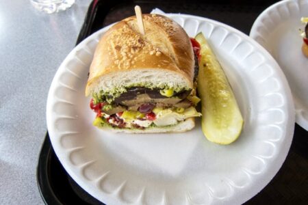 A hearty sandwich with various fillings and a pickle spear on a paper plate, likely from a summer lunch program.