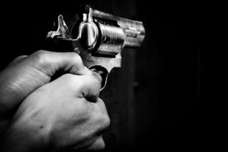 Black and white image of hands holding a revolver, aimed forward against a dark background.