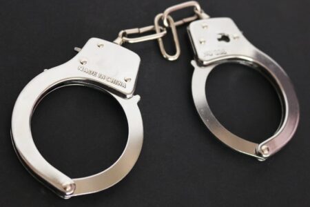 A pair of shiny silver handcuffs rests on a dark, textured surface.