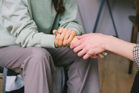 Close-up of two people holding hands, one wearing a green sweatshirt, symbolizing support or comfort.