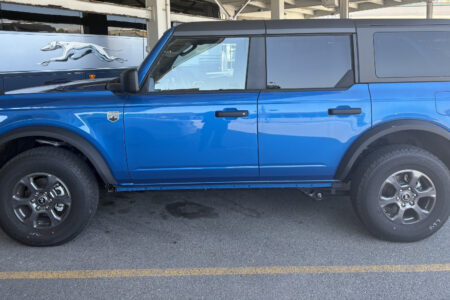 A blue Ford Bronco SUV is parked, with a Greyhound bus visible in the background.