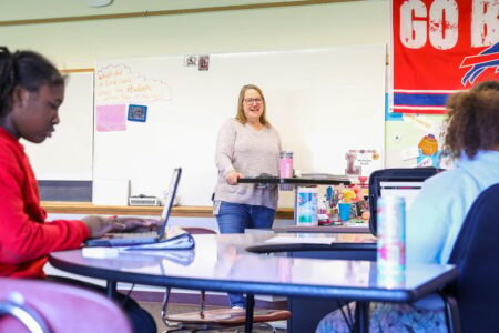 Teacher Alayna Shipley smiles in a classroom with students using laptops.