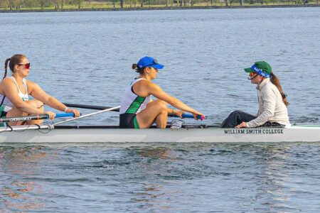 Three William Smith College rowers and a coxswain in a shell on the water.