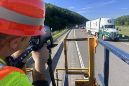 Trooper aims speed gun at traffic in a highway work zone with cones and a semi-truck.