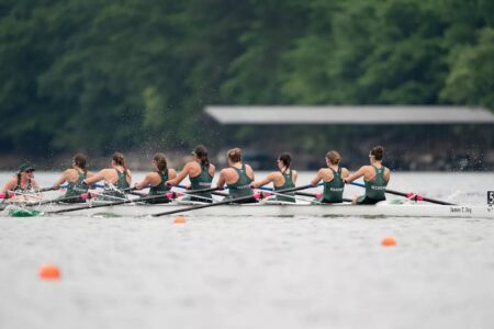 Eight women rowers and a coxswain in a green and white shell on the water, competing during a race.