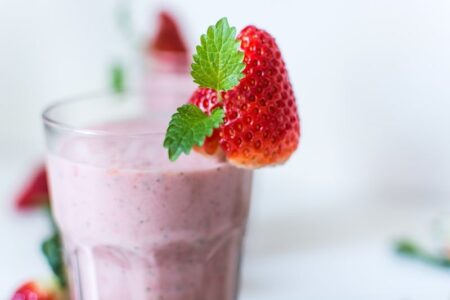 A glass of strawberry smoothie garnished with a fresh strawberry and mint leaf.