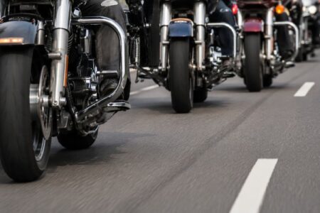 A line of motorcycles from the Red Knights Rally riding on a road, seen from a low angle, with chrome details visible.